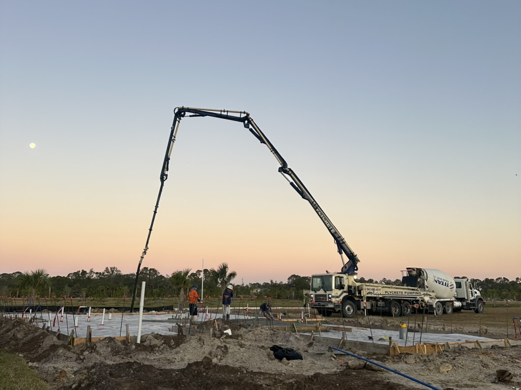 Concrete pump truck pouring a foundation at sunrise.